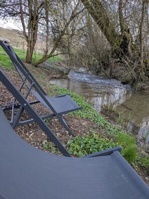 Un endroit pittoresque au bord de la riviĂšre, avec une chaise et une table, entourĂ© dâarbres et de verdure.