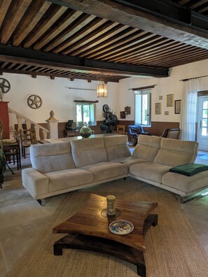 Un salón con un amplio sofá seccional color beige, una mesa de centro de madera y un techo rústico con vigas a la vista.