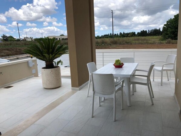 Eine Terrasse im Freien mit einem weißen Tisch und Stühlen, einer Topfpflanze und Blick auf die Landschaft.