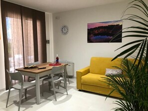 Ein Essbereich mit einem Holztisch und Stühlen, einem gelben Sofa, einer Uhr und einem Landschaftsbild an der Wand.