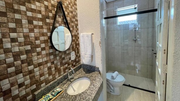 A bathroom with a checkered tile wall, a round mirror, a sink, and a toilet. - Hotel Carmelita (Aparecida)