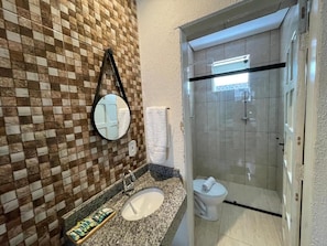 Een badkamer met een wand betegeld met schaakkleurend tegelpatroon, een ronde spiegel, een wastafel en een toilet.