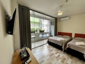 Hotellihuone, jossa on sänky, työpöytä, jossa on kaukosäädin, lasiovi, joka johtaa parvekkeelle, ja seinälle asennettu televisio.