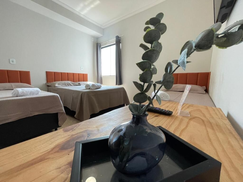 A hotel room with two beds, a wooden desk, a vase with a plant, and a window with curtains.