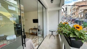 A balcony with a glass door leading to a room, a small table, and a potted plant with sunflowers. - Hotel Carmelita (Aparecida)
