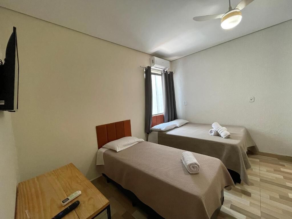 Una habitación con dos camas, una mesa de madera, un televisor y un ventilador de techo.