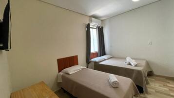 Una habitación con dos camas, una mesa de madera, un televisor y un ventilador de techo.