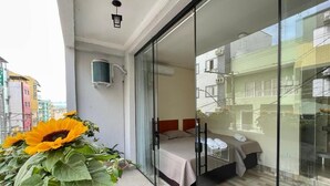 A hotel room with a bed, a glass door leading to a balcony, and a large potted plant with sunflowers.