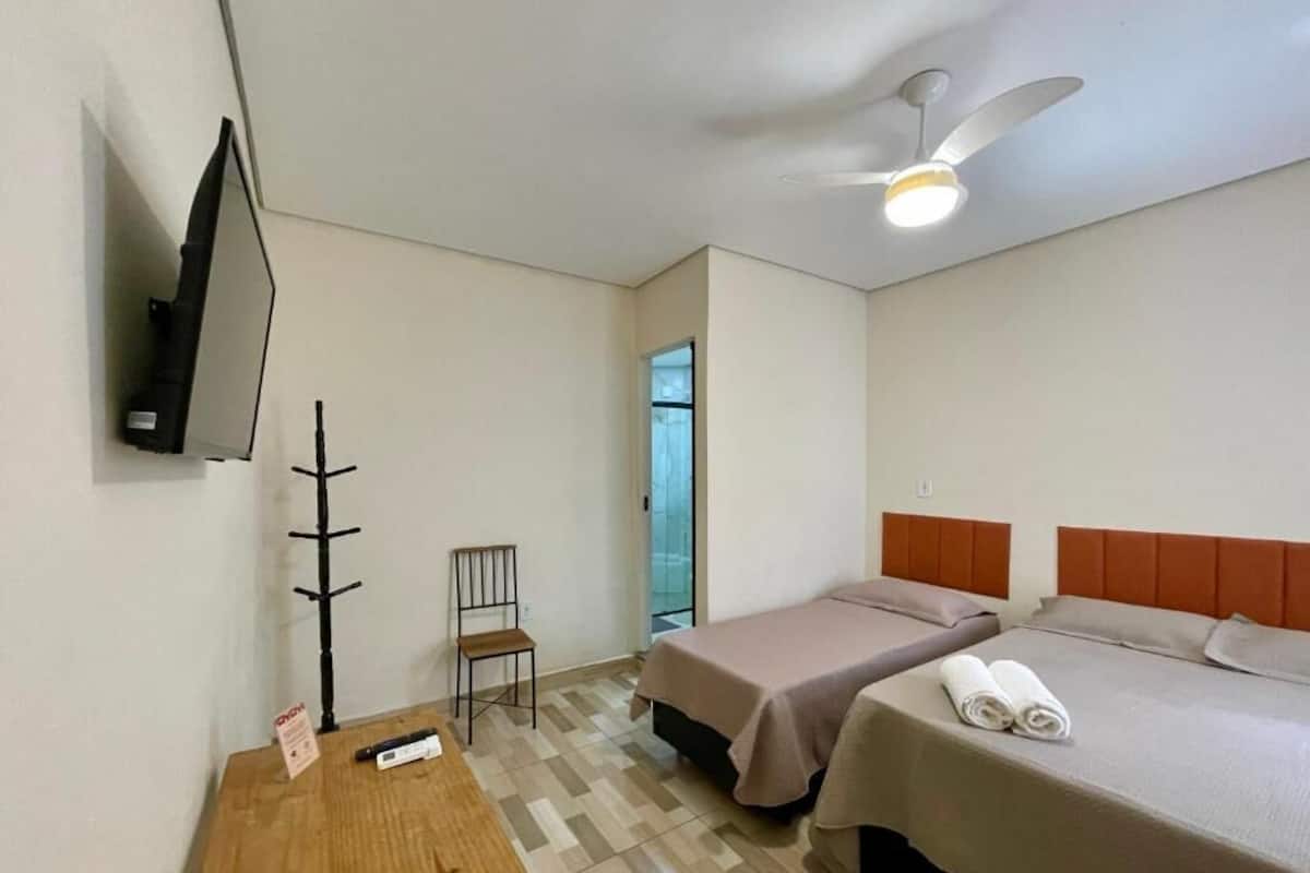 A hotel room with two beds, a TV mounted on the wall, a ceiling fan, and a small table.