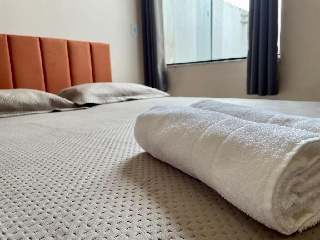 Una cama bien hecha con una toalla blanca, una colcha con textura y un cabecero naranja.
