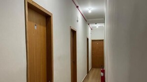 A corridor with wooden doors, a fire alarm, and a tiled floor.