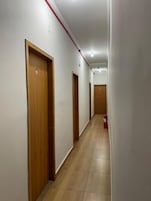 Corredor com portas de madeira, alarme de incêndio e piso ladrilhado.
