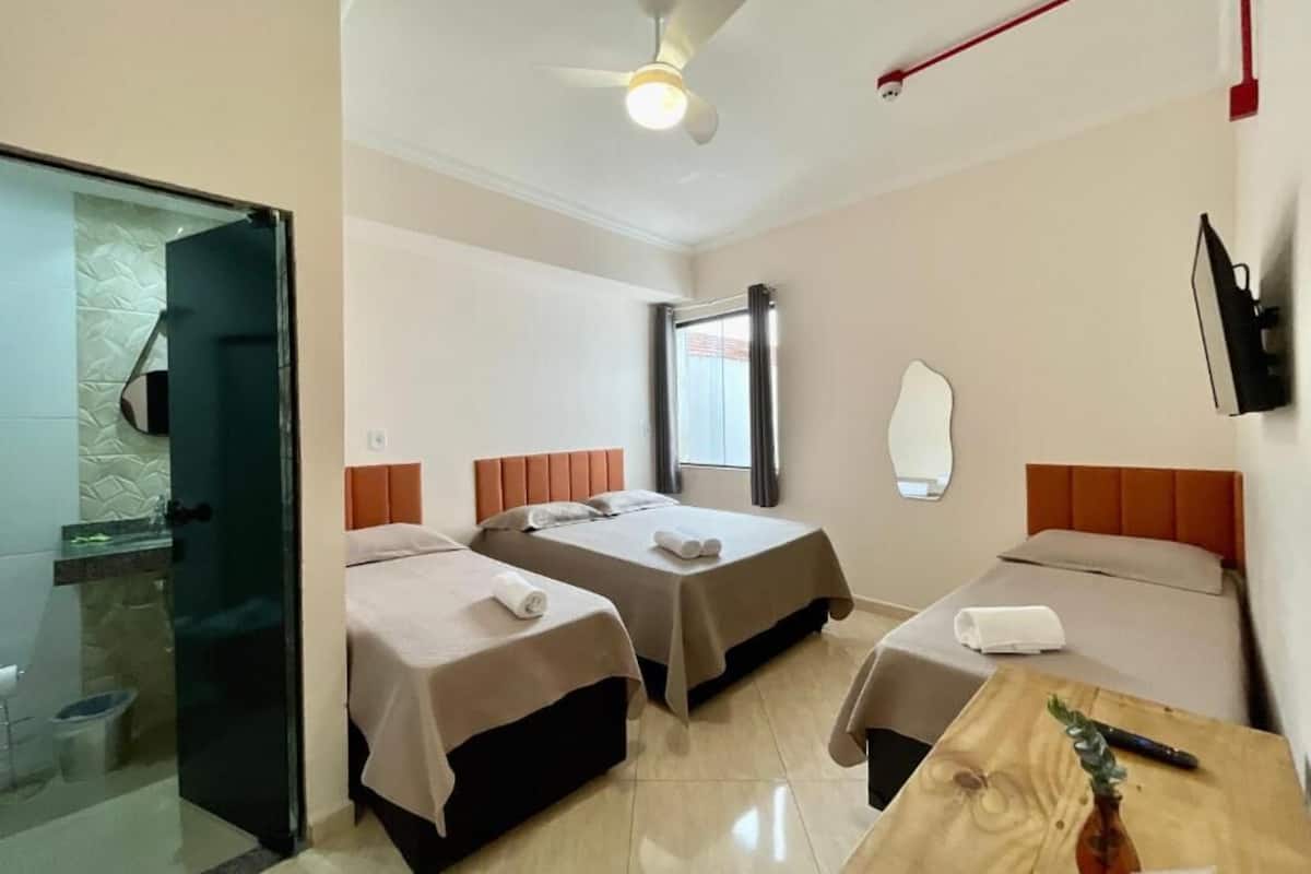 A hotel room with two beds, a ceiling fan, a TV, and a wooden table with a vase.