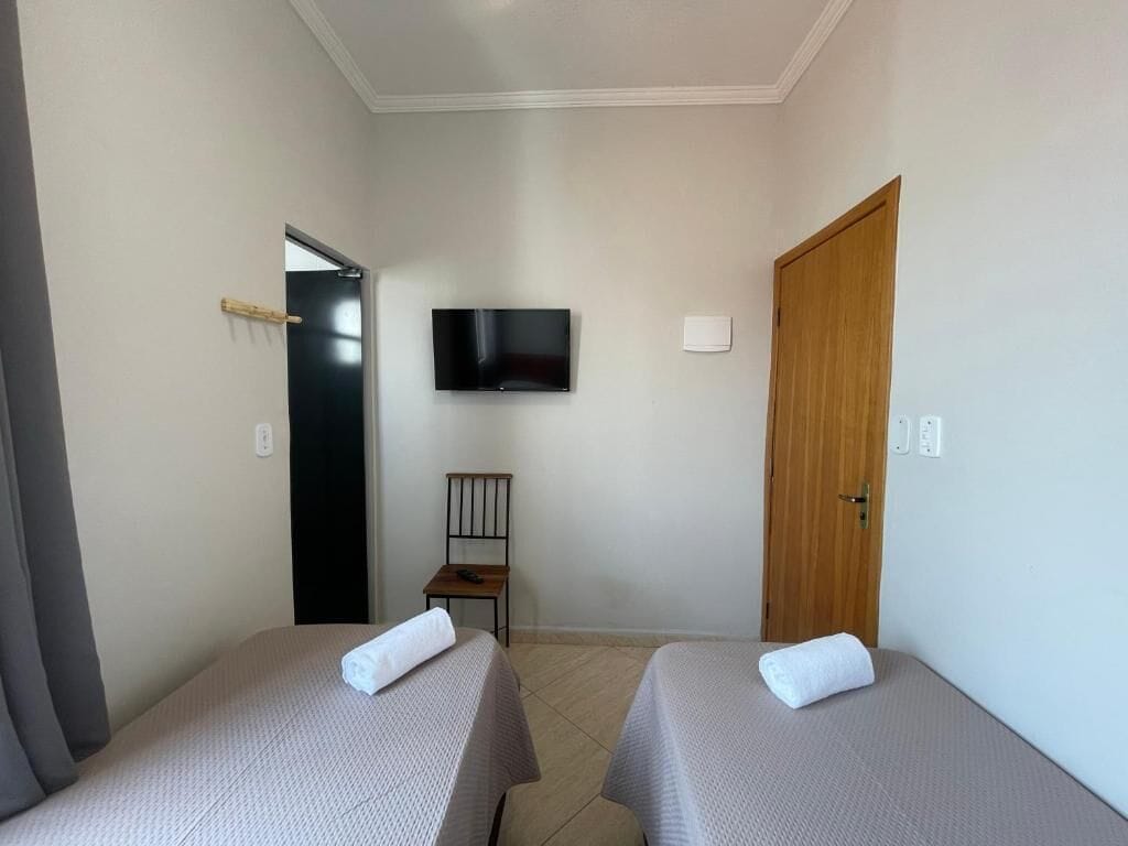 Une chambre d’hôtel avec deux lits, un téléviseur fixé au mur, une porte en bois et une chaise.