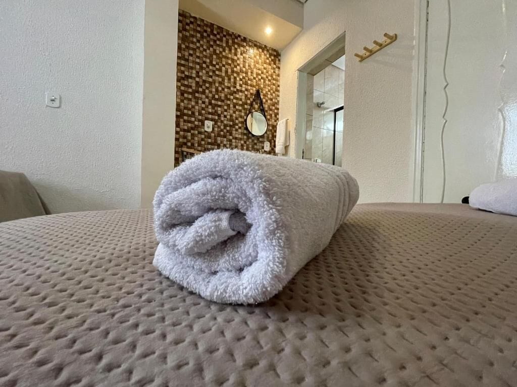 Una cama bien hecha con una toalla enrollada, una pared con textura y un espejo.