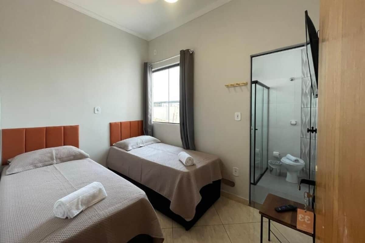 A hotel room with two beds, a shower area, and a small table with a remote control.