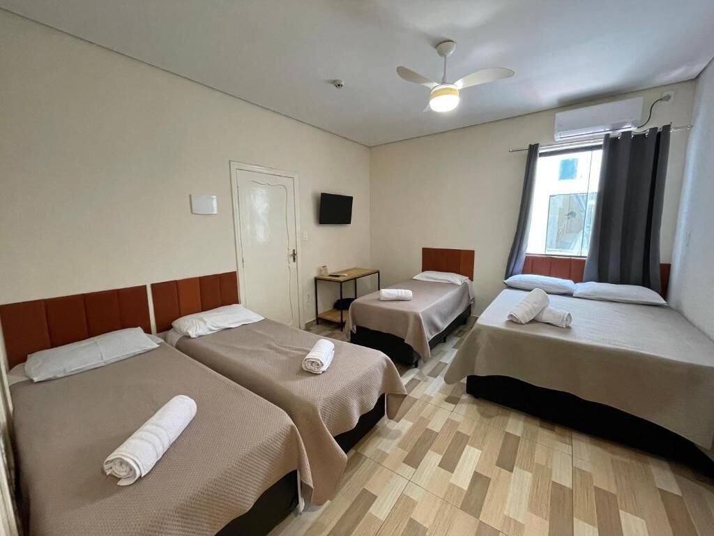 Et hotelværelse med tre senge, en ventilator, et fladskærms-TV og et vindue med gardiner.