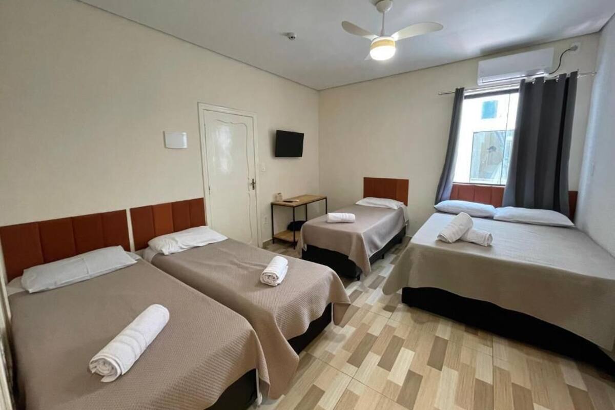 A hotel room with three beds, a ceiling fan, a flat-screen TV, and a window with curtains.