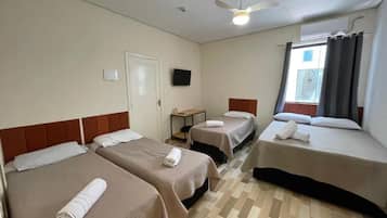 A hotel room with three beds, a ceiling fan, a flat-screen TV, and a window with curtains.