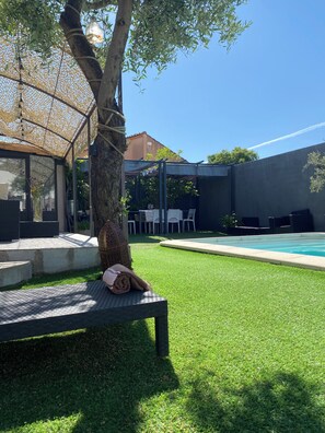 Un espace aménagé au bord de la piscine, comprenant un banc, une pergola et une table avec des chaises.