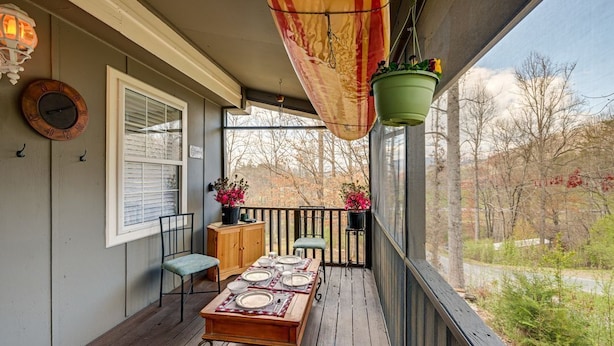 Una terraza de madera con una mesa lista para comer, una planta colgante y vistas a árboles y una carretera.