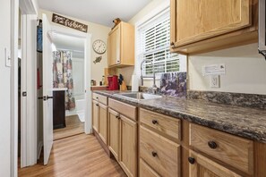 A kitchen with wooden cabinets, a granite countertop, a clock, and a window with blinds. - Papa Bear Cabin Near Cherokee with Shared Hot Tub (Whittier)