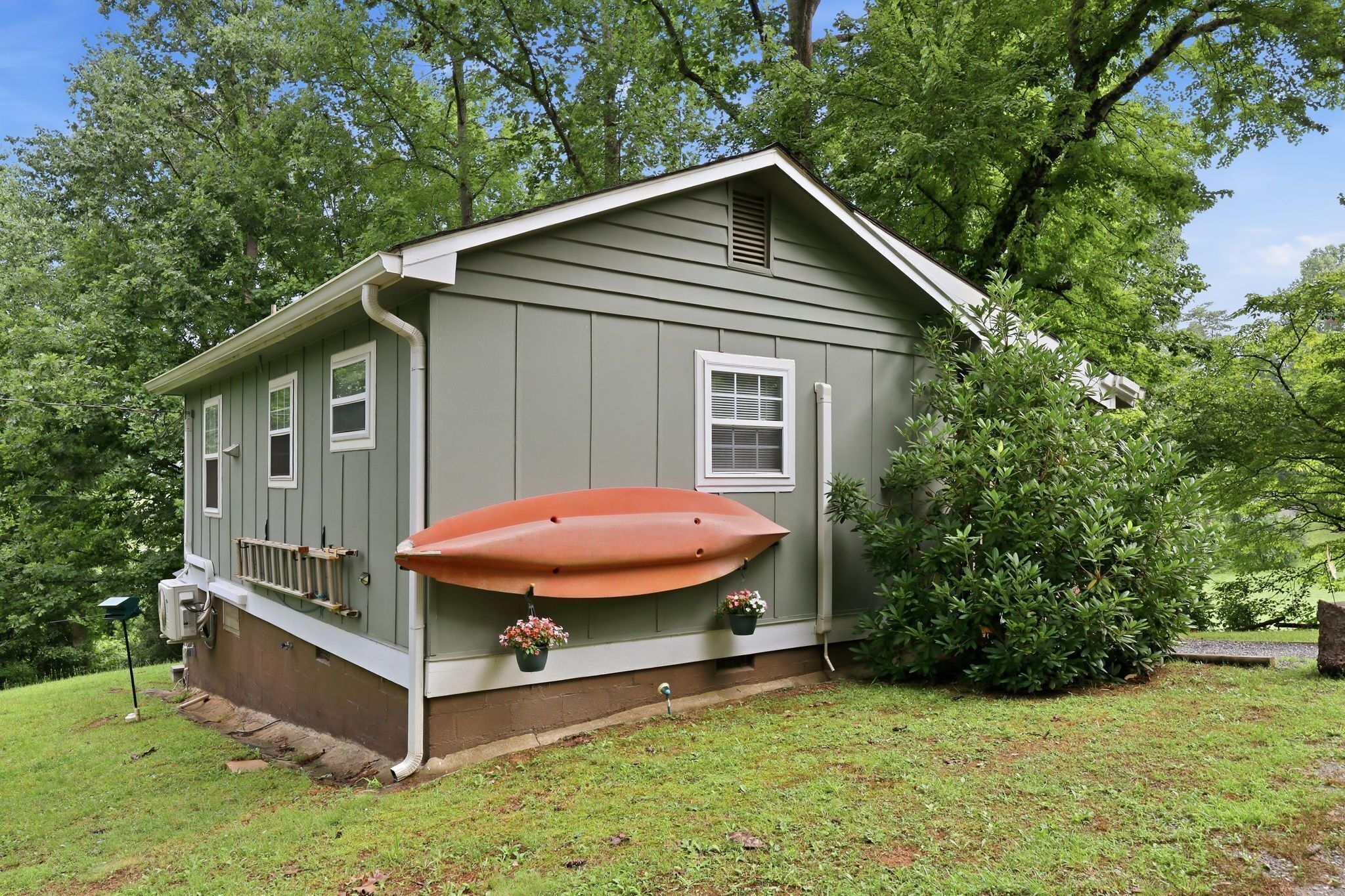 A small house with a garage, a red boat on the side, and a small garden with potted plants.