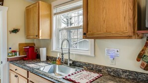 Una cocina con gabinetes de madera, encimera de granito, pileta de acero inoxidable y ventana con persianas.