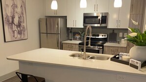 Una cocina moderna con electrodomésticos de acero inoxidable, iluminación colgante y una isla central con taburetes.