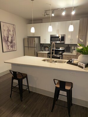 Een moderne keuken met roestvrijstalen apparatuur, hanglampen en een centraal eiland met krukken.