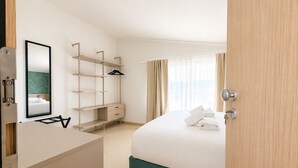 Una habitación de hotel con cama, escritorio, espejo, armario y ventana con cortinas.