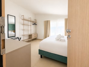 Hotelkamer met een bed, bureau, spiegel, kast en raam met gordijnen.