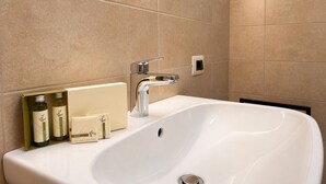 Un baño moderno con un lavamanos grande blanco, un grifo cromado y un espejo montado en la pared. Hay artículos de aseo en el borde del lavamanos.