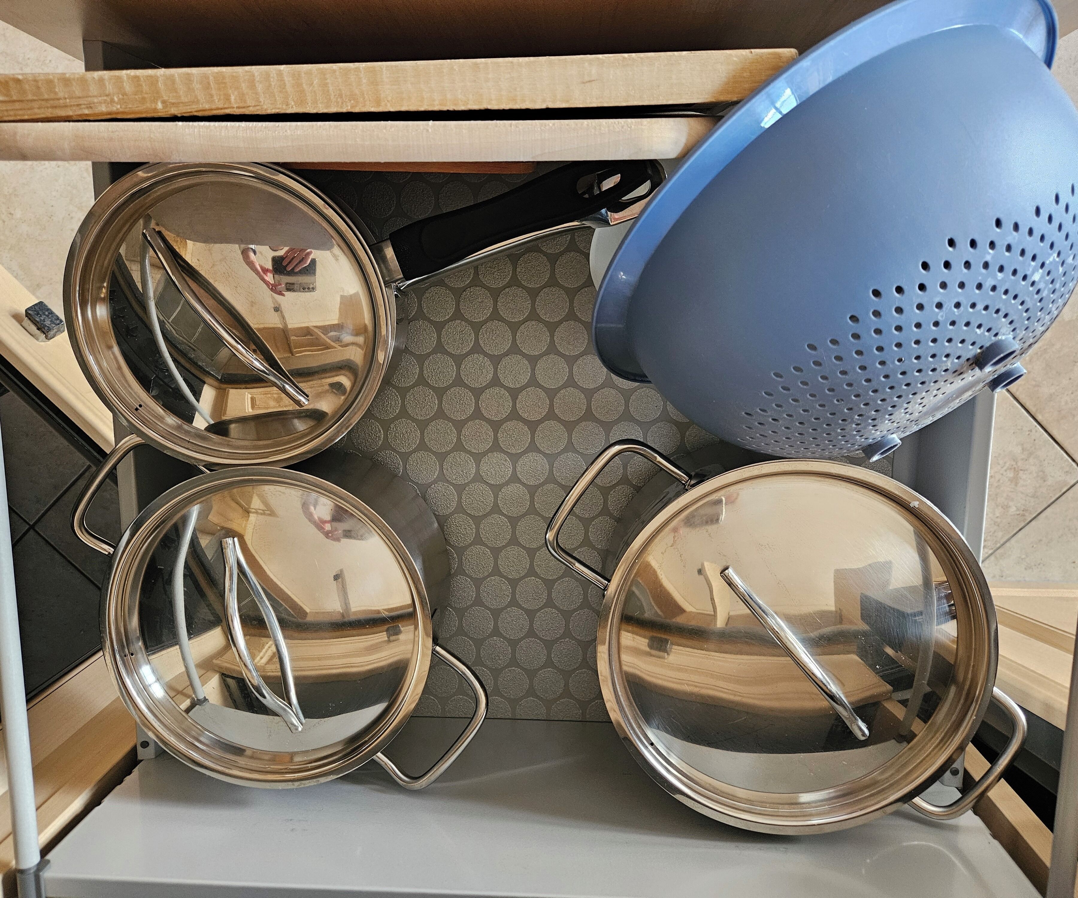 Une cuisine avec des casseroles en acier inoxydable et une passoire bleue.