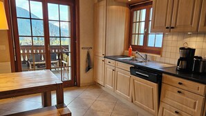 A kitchen with wooden cabinets, a black countertop, a dishwasher, and a window with a view of mountains. - Spacious central 5-room apartment (Leysin)
