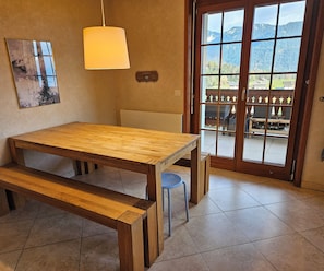 A wooden table with benches, a hanging light fixture, a wall-mounted plaque, and a view through a glass door.