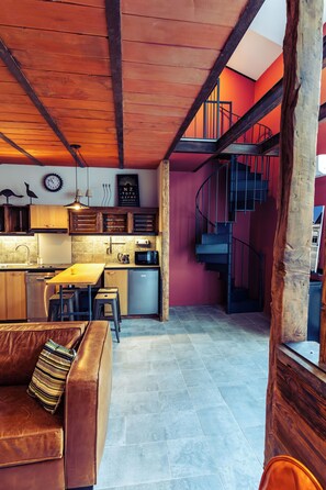 A modern kitchen with wooden beams, a spiral staircase, and a dining area with a leather couch.
