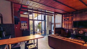 Una cocina moderna con una mesa de madera, taburetes de bar, un sofá de cuero y un televisor grande.