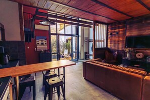 A modern kitchen with a wooden table, bar stools, a leather sofa, and a large TV.