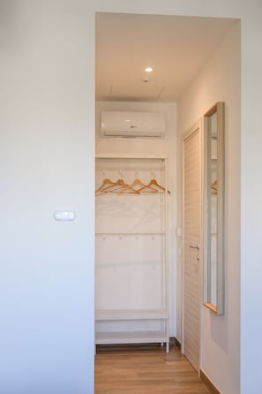 Un pasillo con un armario blanco, perchas de madera, un espejo y un aire acondicionado instalado en el techo.