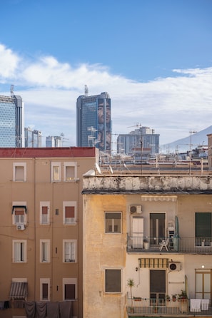 Um edifício com vários andares, varandas, um aparelho de ar condicionado visível e um pequeno jardim.