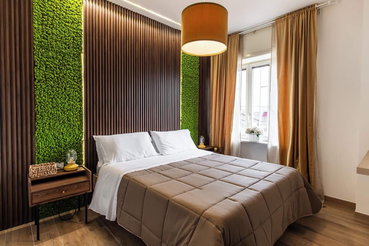 Una habitación de hotel moderna con una cama, una mesita de noche, una pared verde y una ventana con cortinas.