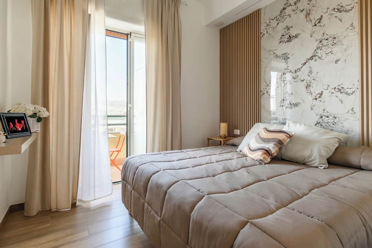 Un dormitorio con una cama grande, una mesita de noche, una silla y vistas al exterior.