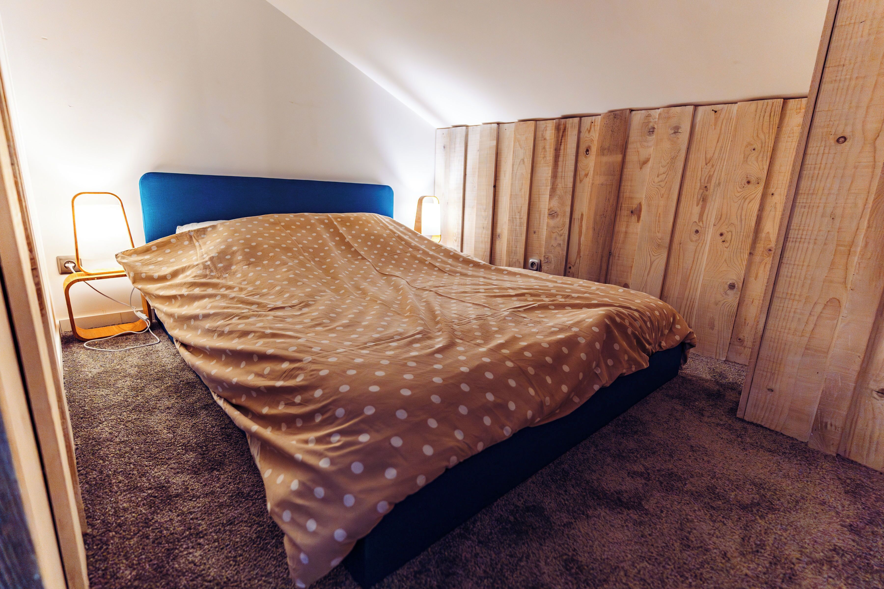 Une chambre à coucher avec un lit, une tête de lit en bois, une table de chevet et une lampe.