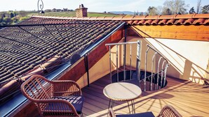 Une terrasse en bois avec des chaises et une table en osier, un toit en tuiles et une vue sur la campagne.