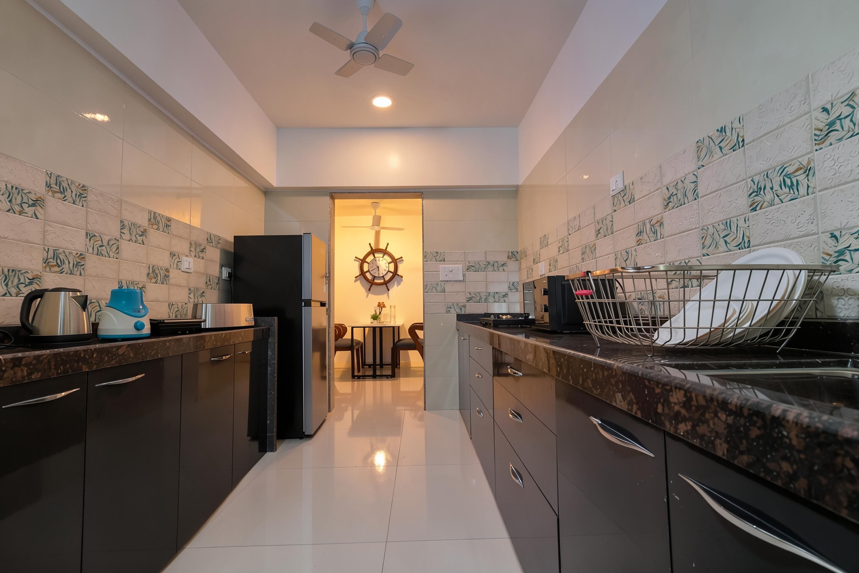 Una cocina moderna con armarios oscuros, encimera de mármol y un comedor con mesa y sillas.