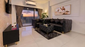 A modern living room with a black sofa, a glass coffee table, and a large window with curtains. - Santacruz Homesuites - Gagal Home (Mumbai)