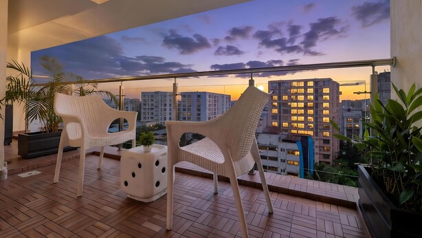 A balcony with two white chairs, a small table, and potted plants. - Santacruz Homesuites - Gagal Home (Mumbai)