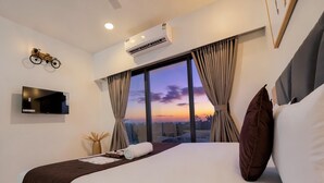 A hotel room with a large bed, a mounted TV, an air conditioner, and a window with curtains. - Santacruz Homesuites - Gagal Home (Mumbai)