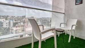 A balcony with two white plastic chairs, a small round table, and a view of a cityscape through a mesh screen. - Santacruz Homesuites - Gagal Home (Mumbai)